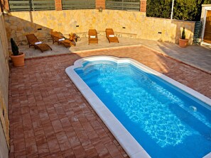A swimming pool with a stone wall and tiled flooring, surrounded by lounge chairs and a small table. - Family Home Iskra (Bulic)