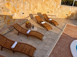 A stone wall with wooden lounge chairs and a small table with a bottle and glasses. - Family Home Iskra (Bulic)