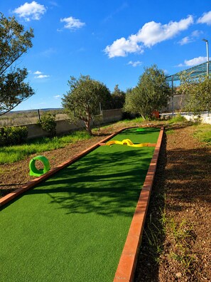 A miniature golf course with a green artificial turf, a yellow curved path, and a green circular obstacle. - Family Home Iskra (Bulic)