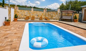 A swimming pool with a stone wall and lounge chairs.