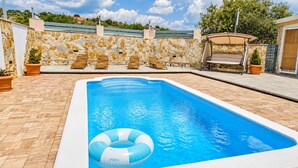 A rectangular swimming pool with a stone wall and a clear blue sky in the background. - Family Home Iskra (Bulic)