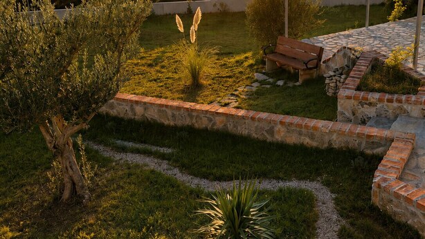 A garden with a stone pathway, a bench, and a view of the sunset over a hilly landscape. - Family Home Iskra (Bulic)