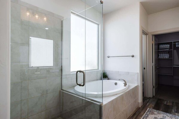 Un baño moderno con ducha envuelta en vidrio, una bañera grande y un vestidor.