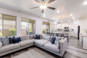 A modern kitchen with white cabinets, a dining area with a gray sofa, and a ceiling fan. - Adventure & Comfort | Community Pool | 344 Puerta (Washington)