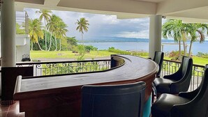 Un mostrador de recepción curvo con vistas a un paisaje costero, incluyendo palmeras y una masa de agua.