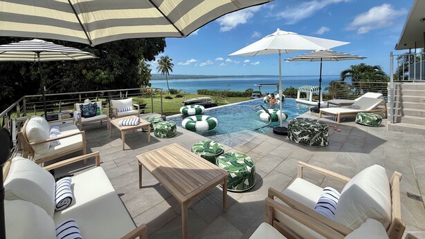 Zona de piscina con sillones de descanso, sombrillas y vista al océano.