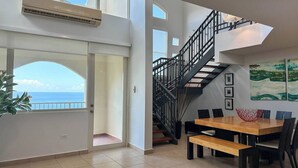 Amplia sala de estar con un gran comedor, una escalera y vista al océano.