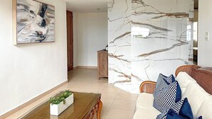 A modern living room with a marble accent wall, a dining area with a glass-top table, and a large abstract painting.