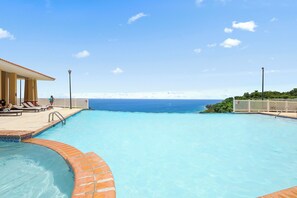 A swimming pool with clear blue water, a tiled deck, and a view of the ocean.