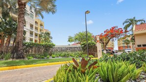 A landscaped area with a paved walkway, palm trees, and a building with balconies.