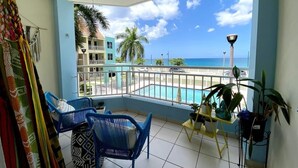 Un balcone con vista su una piscina e l'oceano, sedie blu e piante in vaso.