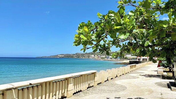 Une promenade en bord de mer, avec une allée en béton, une clôture en bois et une vue sur la mer et les bâtiments situés au loin.