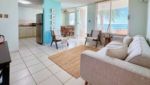 Un salon comprenant un canapé, une table basse et un coin repas avec des chaises et une table. Il y a également une cuisine équipée d’un réfrigérateur et d’un évier.
