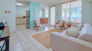 Un grand espace de vie comprenant un canapé, une table à manger avec des chaises et un coin cuisine équipé d’un réfrigérateur.