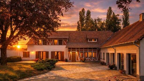 Un bâtiment traditionnel avec un chemin de pierre menant à l’entrée, entouré d’arbres et avec un coucher de soleil en arrière-plan.