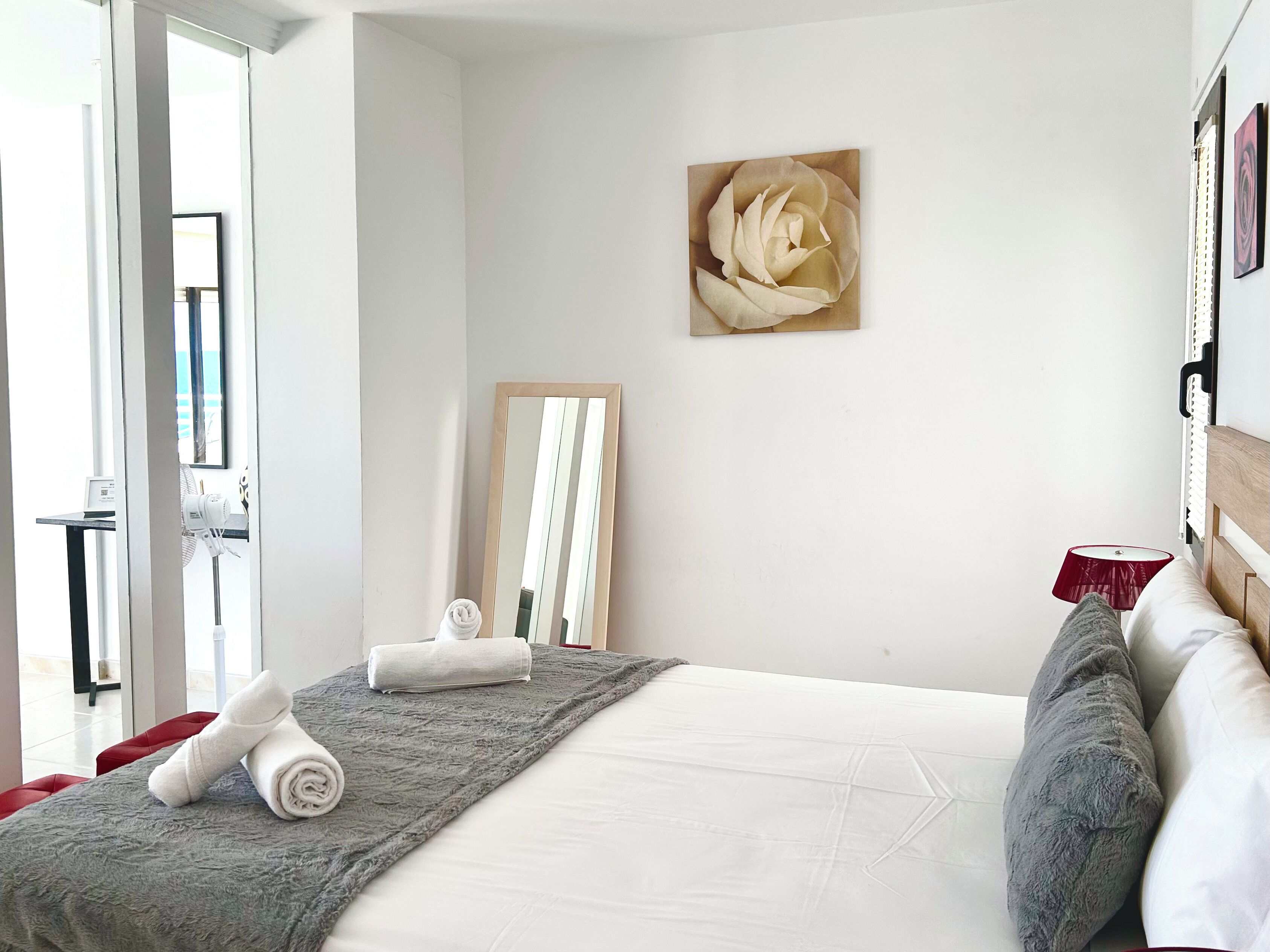 Une chambre d’hôtel avec un lit, un miroir, un tableau et une lampe rouge.