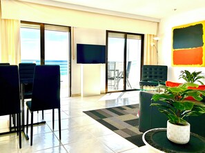 A modern living room with a large TV, a sofa, and a dining area with chairs.