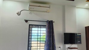 Une chambre dotée d’une fenêtre, d’un appareil de climatisation, d’une télévision et d’une armoire en bois.
