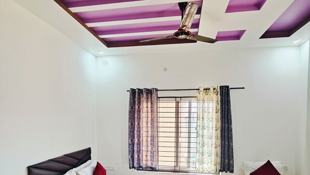 Une chambre à coucher avec un lit, des tables de chevet, un ventilateur de plafond et une fenêtre avec des rideaux.