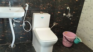 Une salle de bain avec un lavabo blanc, des toilettes et un seau rose.