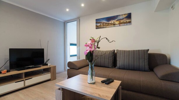 A modern living room with a flat-screen TV, a wooden coffee table, a sofa, and a vase with flowers. - Apartman Mrkonjic-Pula (Pula)