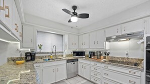 A modern kitchen with white cabinets, granite countertops, a built-in microwave, and a ceiling fan. - This house is a 3 bedroom(s), 2 bathrooms, located in Richardson, TX. (Richardson)