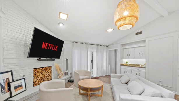 A modern living room with a flat-screen TV displaying 'NETFLIX', a round wooden coffee table, a white sofa, and a kitchen area with white cabinets. - This house is a 3 bedroom(s), 2 bathrooms, located in Richardson, TX. (Richardson)