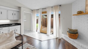 A spacious living area with a kitchen, a sliding glass door to the backyard, and a white brick fireplace.
