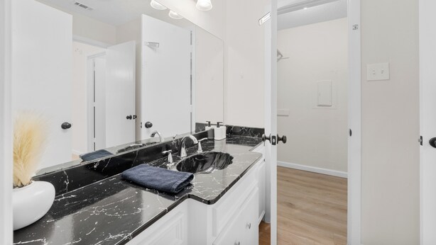 A bathroom with a black marble sink, white cabinets, and a large mirror.