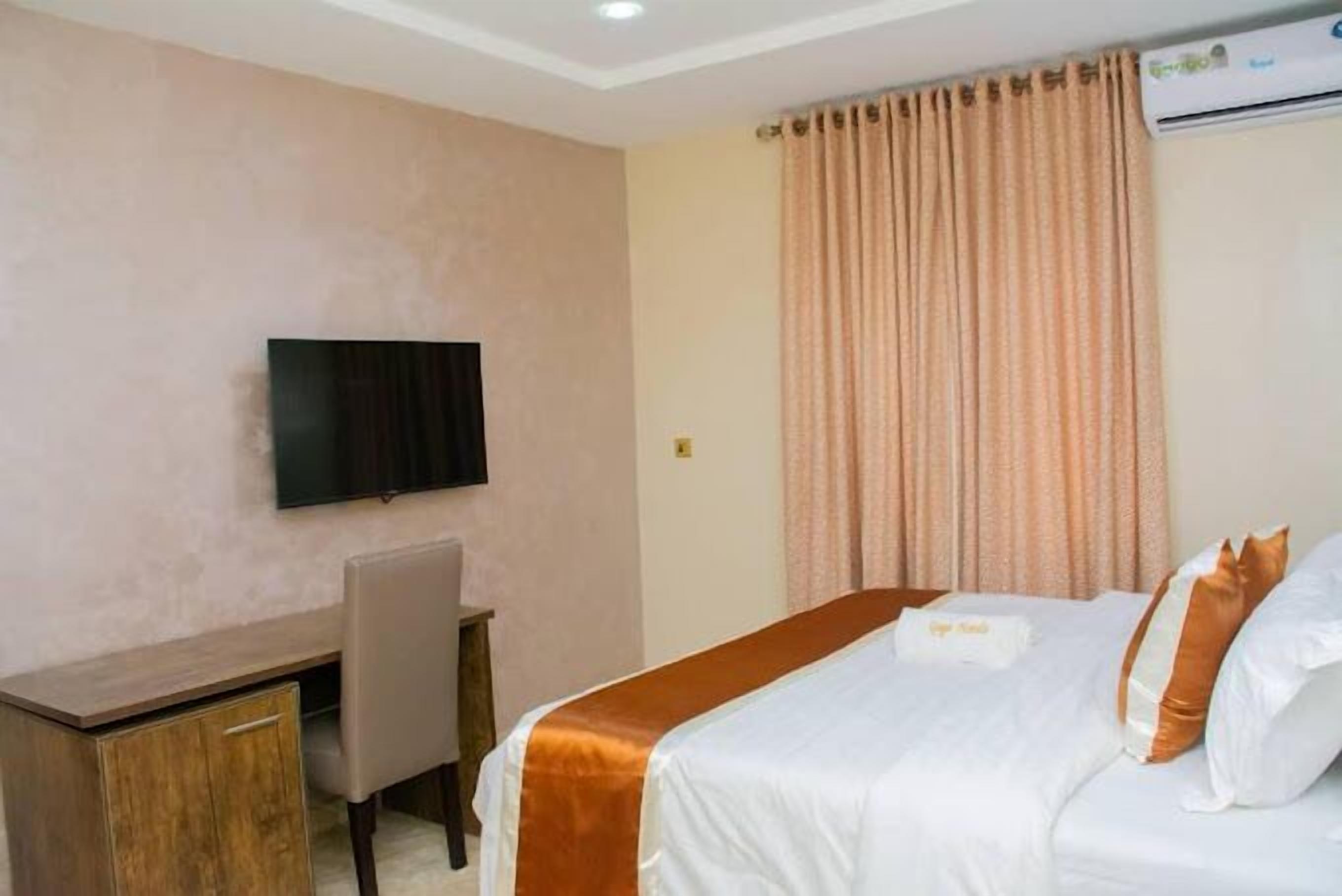 A hotel room with a bed, a desk, a chair, a television, and a window with curtains.