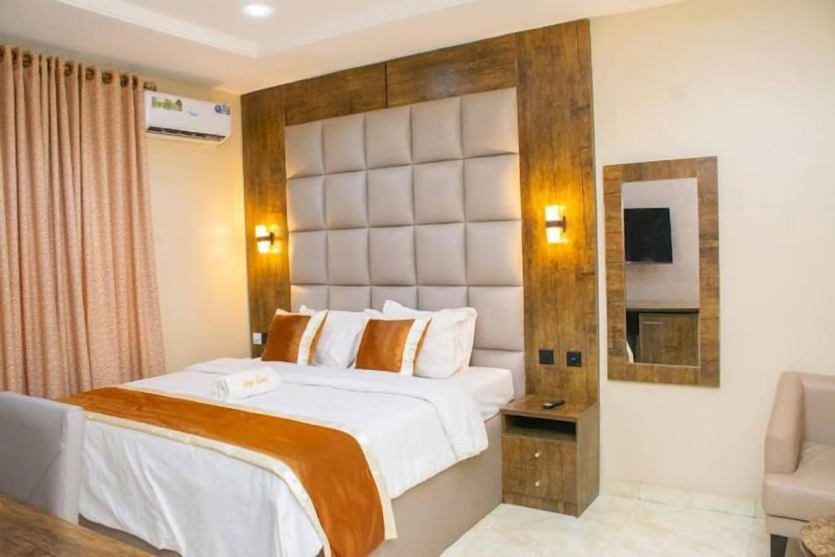 Une chambre d’hôtel avec un grand lit, une tête de lit en bois, une table de chevet, un téléviseur fixé au mur et une fenêtre avec des rideaux.