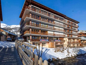 A multi-story hotel with balconies, a sign for 'INTERSPORT,' and a view of snow-covered mountains.