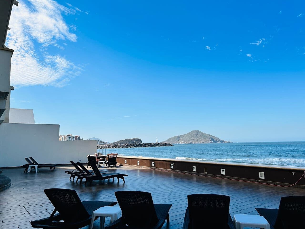 A rooftop terrace with sun loungers and a view of the sea and a distant island.