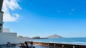 A rooftop terrace with sun loungers and a view of the sea and a distant island.