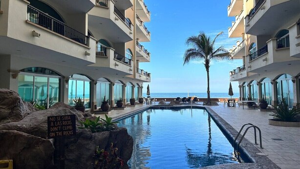 A pool area with a sign warning against climbing on rocks, surrounded by multi-story buildings with balconies and large windows.