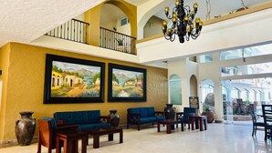 A spacious lobby with a high ceiling, a balcony, and two large landscape paintings.