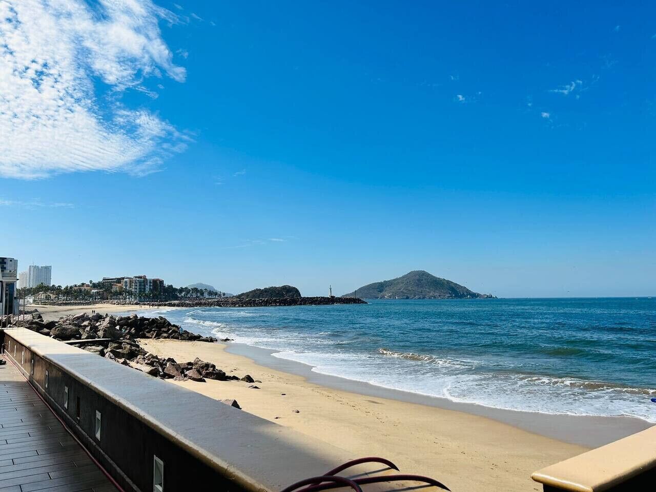 A coastal view with a sandy beach, rocky shoreline, and a distant mountain.