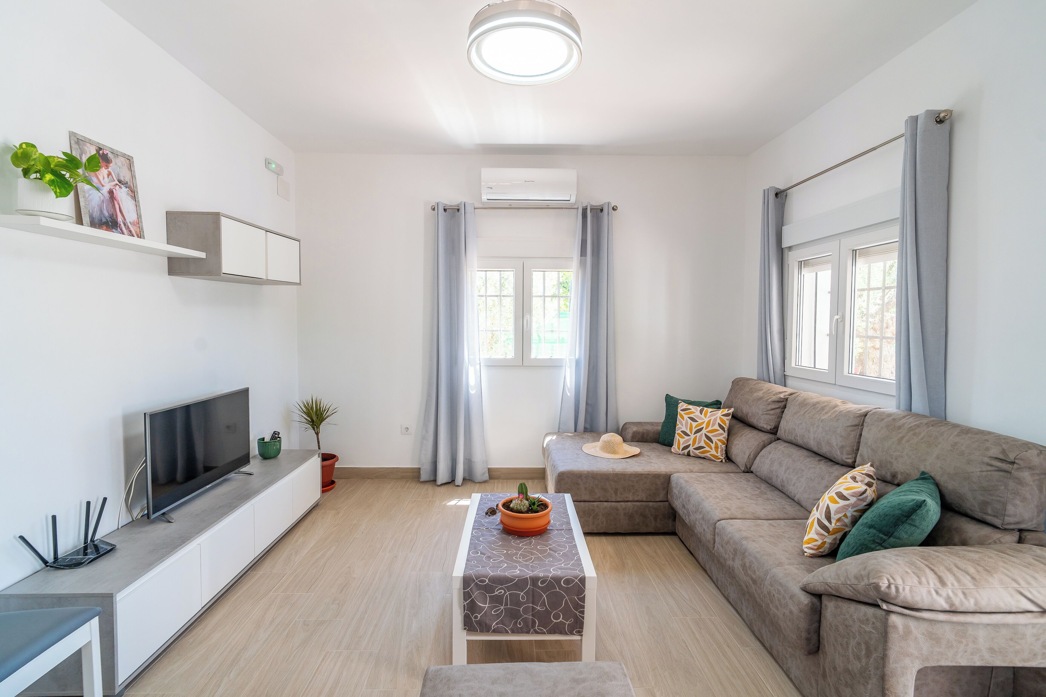 A modern living room with a flat-screen TV, a sofa, a coffee table, and a window with curtains.