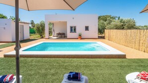 Une piscine dotée d’une terrasse blanche, entourée d’une clôture en bois et d’une pelouse verdoyante.