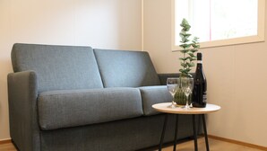 A grey sofa with a small round table beside it, featuring a wine bottle, a glass, and a plant. - Utvika Gård & Camping (Hole)