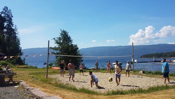 A beach volleyball game on a sandy court with a lake and mountains in the background. - Utvika Gård & Camping (Hole)