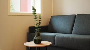 A room with a grey sofa, a small round wooden table with a vase, and a window with blinds. - Utvika Gård & Camping (Hole)