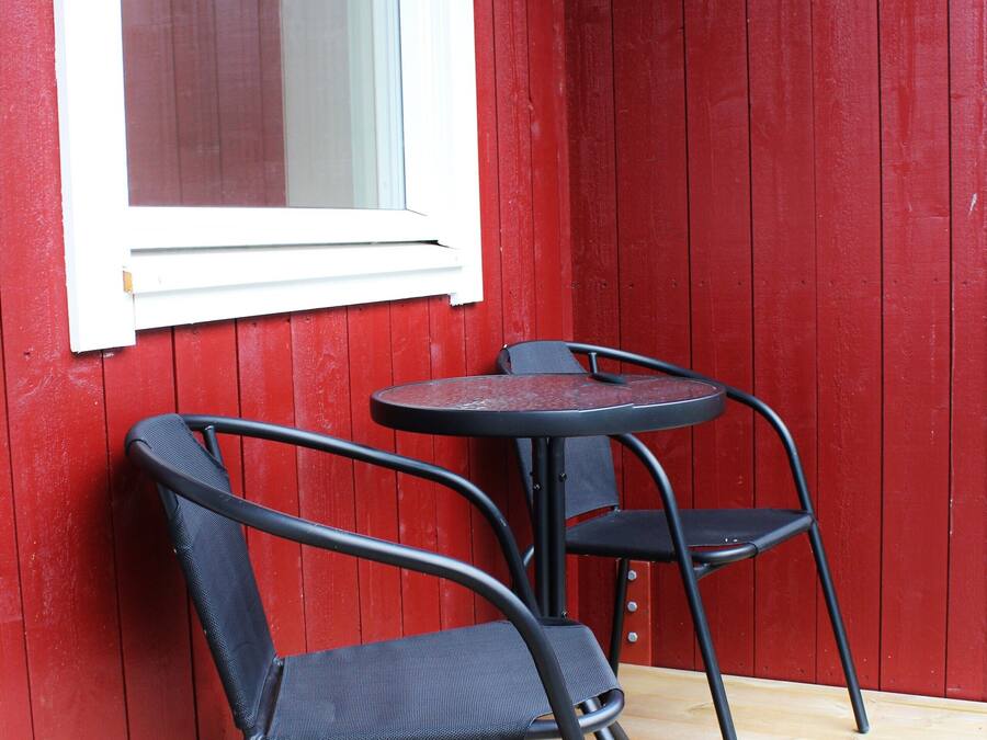 Un pequeño espacio al aire libre con una mesa, dos sillas, una ventana y una pared roja.