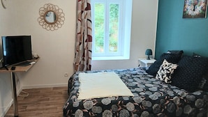 A bedroom with a bed, a desk with a computer, a window with curtains, a wall clock, and a painting.