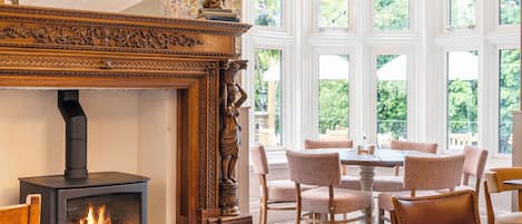 Una habitación con chimenea, una mesa de comedor con sillas y ventanas amplias con vistas a vegetación.