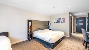 A hotel room with a large bed, a desk with a chair, a small table, and a painting on the wall.