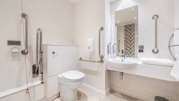 Un baño moderno con inodoro, lavabo y barras de apoyo.