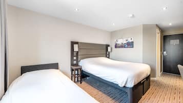 Et hotelværelse med to enkeltsenge, et lille bord, en stol og et billede på væggen.