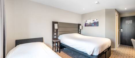 A hotel room with two single beds, a small table, a chair, and a painting on the wall.