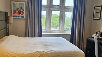 Habitación de hotel con cama, escritorio con silla, ventana con cortinas y un cuadro en la pared.